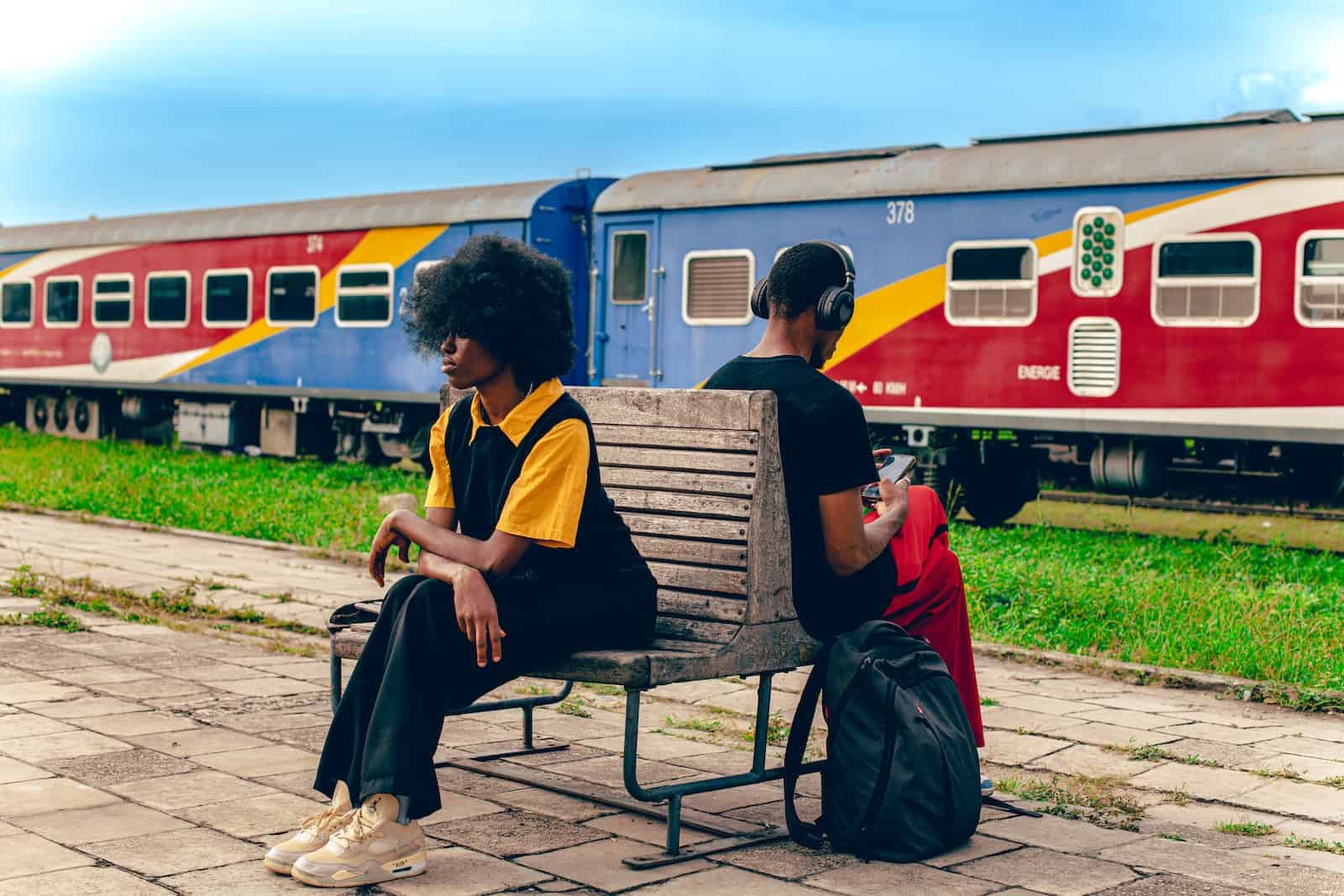 two people sitting on a bench in front of a train